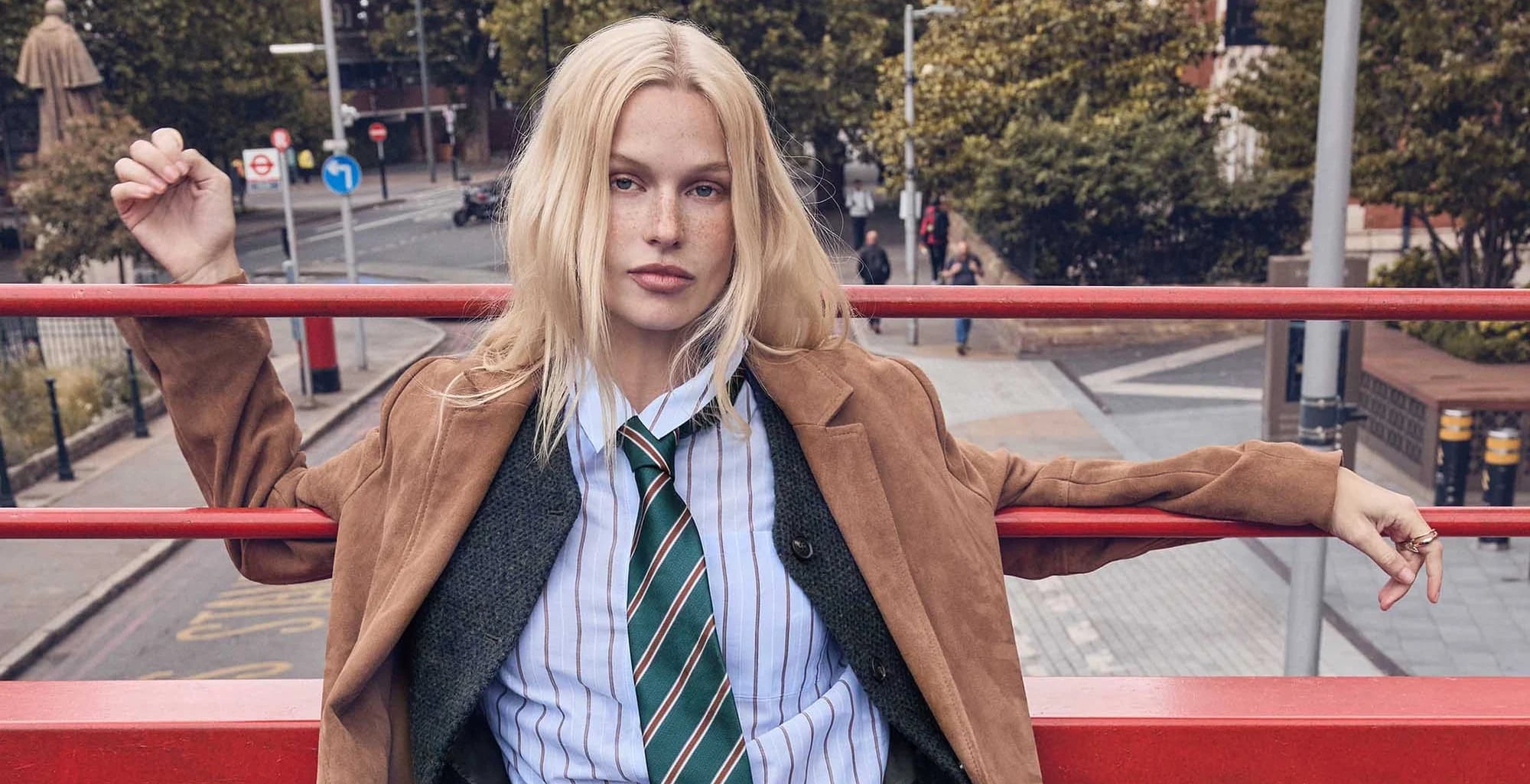 A woman in a suede jacket and striped tie on the top deck of a London bus