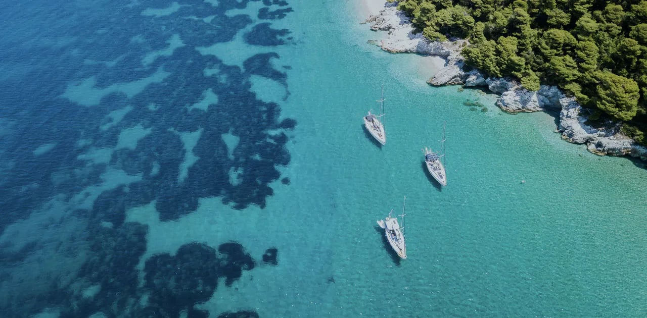 Trois voiliers au mouillage dans une crique aux eaux turquoise, vus du ciel